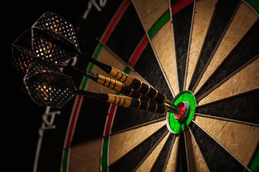 A close up photo of a dart board with three darts in the target. 